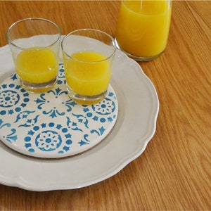 May include: Two glasses of orange juice on a white plate with a blue and white patterned coaster.