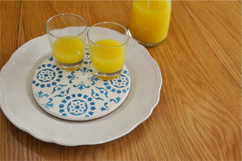 May include: Two glasses of orange juice on a white plate with a blue and white patterned coaster.