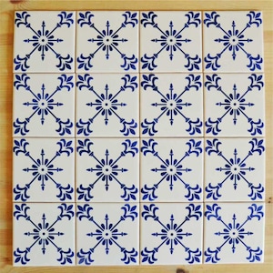 Può includere: Un set di 16 piastrelle in ceramica bianca con un motivo floreale blu. Ogni piastrella presenta un fiore stilizzato con quattro petali e un cerchio centrale. Le piastrelle sono disposte in una griglia 4x4.