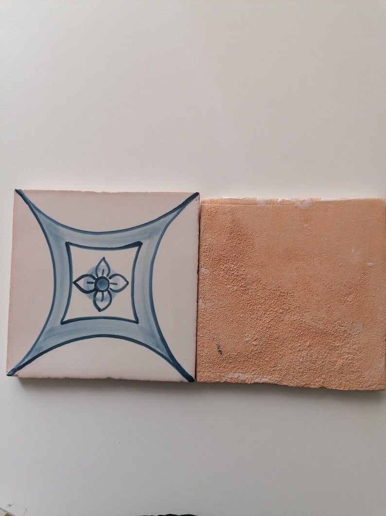 May include: Two ceramic tiles, one with a white background and a blue floral design, the other with a solid light orange background.