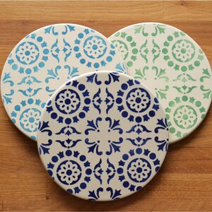 May include: Three round ceramic plates with a white background and blue and green geometric patterns.