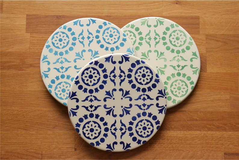 May include: Three round ceramic plates with a white background and blue and green geometric patterns.