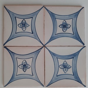 May include: Four white ceramic tiles with a blue and white floral design. Each tile features a stylised flower with four petals and a circle in the centre. The flowers are surrounded by a blue curved design.