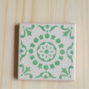 Peut inclure: Un carreau de c&eacute;ramique blanc avec un motif g&eacute;om&eacute;trique vert. Le motif pr&eacute;sente un motif floral central entour&eacute; de cercles, d'&eacute;toiles et de volutes.