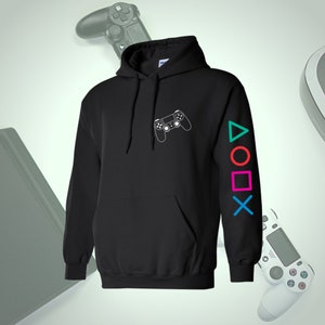 Könnte beinhalten: Schwarzer Kapuzenpullover mit weißer Umrisszeichnung eines Gamecontrollers auf der Brust. Der linke Ärmel zeigt farbige Gamecontroller-Symbole. Ein Hoodie zum Thema Gaming.