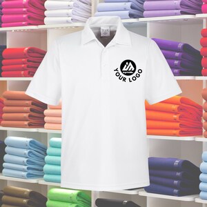 May include: White polo shirt with a black logo that says "ImprintMe" and "YOUR LOGO". The shirt is displayed on a shelf with other folded shirts in various colors.