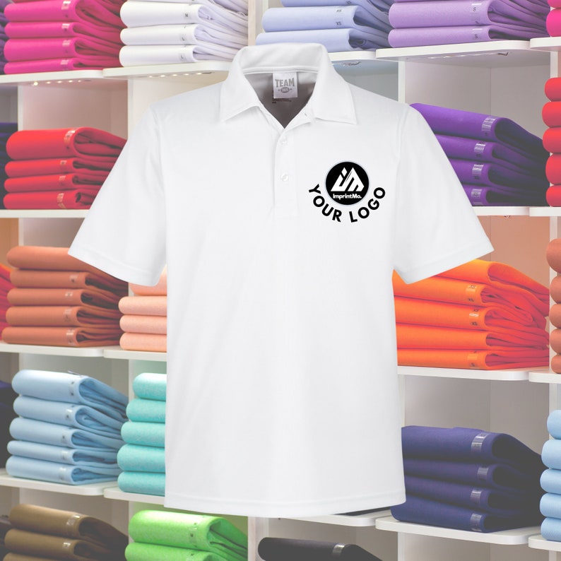 May include: White polo shirt with a black logo that says "ImprintMe" and "YOUR LOGO". The shirt is displayed on a shelf with other folded shirts in various colors.
