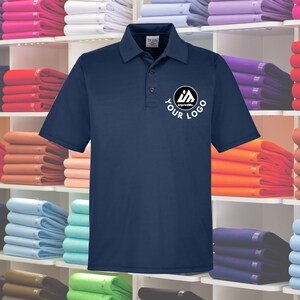 May include: A navy blue polo shirt with a white logo that says "Your Logo" and "ImprintMe" in a circle. The shirt is on a shelf with other shirts in various colors.