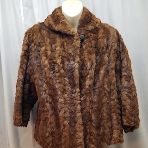 Puede incluir: Chaqueta de piel sintética marrón con cuello redondo y mangas tres cuartos. La chaqueta está abotonada con un solo botón verde oscuro. La prenda se exhibe en un maniquí.