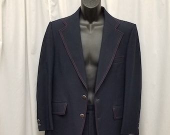 Puede incluir: Un traje azul marino con detalles de costura roja. La chaqueta tiene un cierre de un botón y un bolsillo en el lado izquierdo. El pantalón tiene una pierna recta.