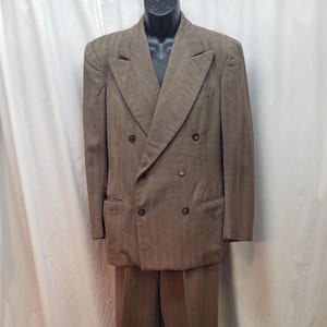 May include: A brown double-breasted suit with a subtle striped pattern. The suit includes a jacket with six buttons and two front pockets, and matching trousers. The suit is displayed on a mannequin against a white backdrop.