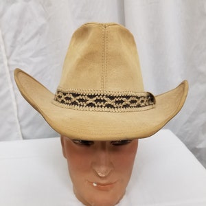 Pode incluir: Um chapéu de cowboy de camurça bege com uma faixa trançada marrom e bege.