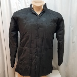 May include: Black quilted jacket with a mandarin collar and button-down front. The jacket has two front pockets and a subtle pattern. The collar has a white trim. The jacket is displayed on a mannequin.
