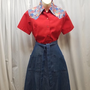 May include: A red short-sleeved shirt with a patterned collar and a denim skirt. The collar features a colorful geometric design. The skirt has two front pockets and a matching belt. The outfit is displayed on a mannequin.