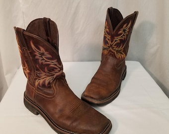 Könnte beinhalten: Ein Paar braune Cowboy-Stiefel aus Leder mit aufwendigen Stickereien am Schaft. Die Stiefel haben eine quadratische Spitze und eine robuste Laufsohle.