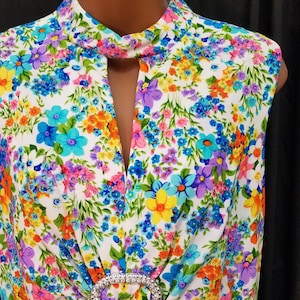 May include: A sleeveless white dress with a colorful floral print. The dress has a high neckline with a keyhole opening and a jeweled belt.