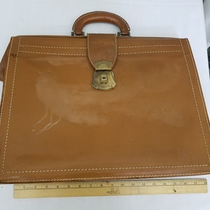 May include: A brown leather briefcase with a brass lock and handle. The briefcase has a stitched border and is in good condition.