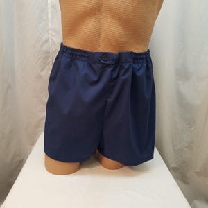 Può includere: Pantaloncini blu navy con elastico in vita e chiusura con un solo bottone. I pantaloncini sono realizzati in un tessuto liscio e tinta unita. L'indumento è esposto su un manichino.