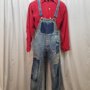 May include: A vintage denim overall set with a red long-sleeve shirt. The overalls have blue patches and suspenders. The red shirt has a white collar and button-down front. The outfit is displayed on a mannequin.