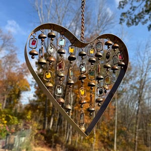 Handcrafted heart wind chime featuring colorful hanging dangles and decorative metal bells with a beautiful flamed finish. Metal wind chimes outdoor designed for garden decor, patio accents, porch decoration, balconies, fences, and backyard landscapes. Heart-shaped hanging garden ornament creates gentle, relaxing sounds while adding artistic charm to outdoor spaces. Perfect farmhouse decor, metal garden art, yard art, housewarming gift, romantic garden decor, and year-round outdoor decoration.