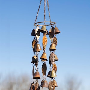 May include: A bronze-colored wind chime with multiple rows of small bells and leaf-shaped accents. The chime hangs from a circular ring and chain, creating a decorative outdoor accent. The bells and leaves have a rustic, weathered appearance.
