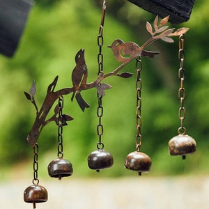 May include: A metal wind chime with a tree branch design and two birds. The chime has five bells, each with a different size and shape.