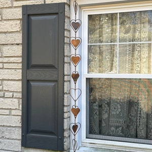 May include: A vertical hanging decoration consisting of a series of interconnected metal hearts. The chain features alternating solid copper-toned heart shapes and open wire heart outlines, suspended by a thin metal hook at the top.