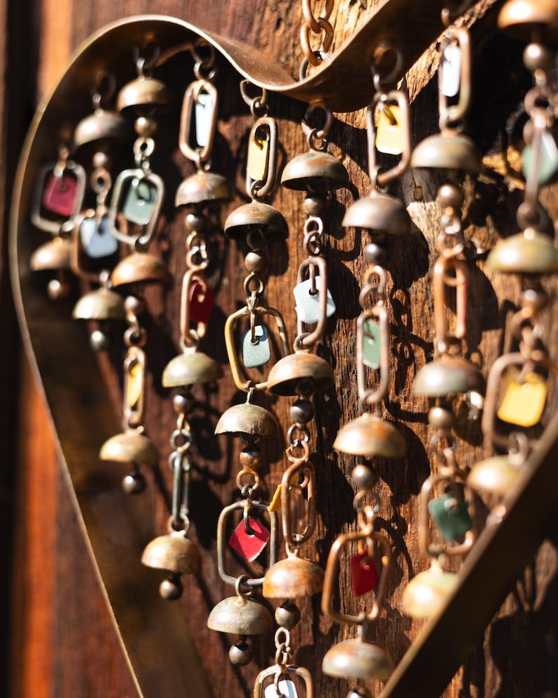 Handcrafted heart wind chime featuring colorful hanging dangles and decorative metal bells with a beautiful flamed finish. Metal wind chimes outdoor designed for garden decor, patio accents, porch decoration, balconies, fences, and backyard landscapes. Heart-shaped hanging garden ornament creates gentle, relaxing sounds while adding artistic charm to outdoor spaces. Perfect farmhouse decor, metal garden art, yard art, housewarming gift, romantic garden decor, and year-round outdoor decoration.