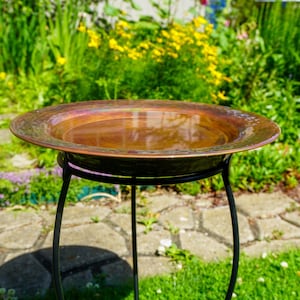 Hammered copper round birdbath with iridescent finish on curved metal stand.