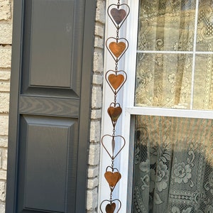 May include: A vertical hanging decoration featuring a series of interconnected metal hearts. The hearts are crafted from thin wire frames with solid copper-toned metal inserts, linked together by small metal chains to form a long, dangling ornament.