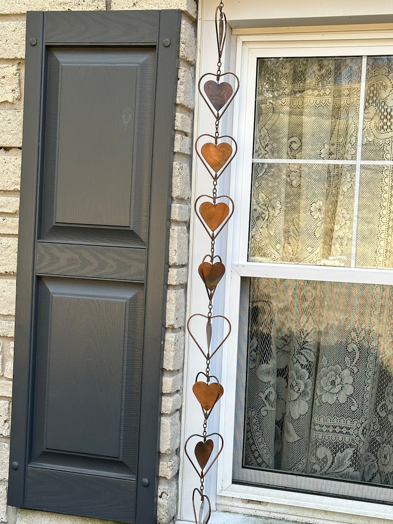 May include: A vertical hanging decoration featuring a series of interconnected metal hearts. The hearts are crafted from thin wire frames with solid copper-toned metal inserts, linked together by small metal chains to form a long, dangling ornament.
