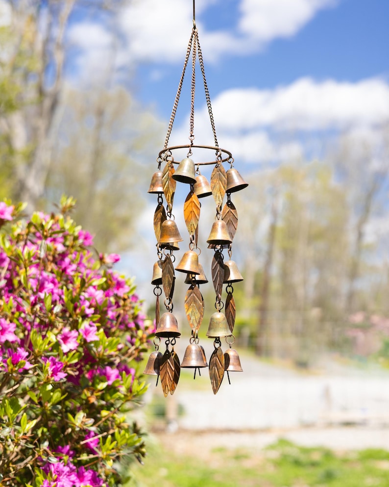 Single tiered metal wind chime with rustic copper finish featuring decorative hanging bells and leaf accents displayed in an outdoor garden setting. Handcrafted wind chimes outdoor for porch, patio, backyard, balcony, and garden decor. Metal wind chime adds soothing sounds and elegant movement to outdoor spaces. Rustic copper wind chime makes a beautiful gardener gift, gifts for mom, housewarming gift, outdoor garden decor, metal garden art, and yard decoration for every season.