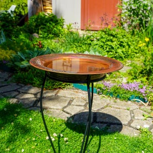 Hammered copper round birdbath with iridescent finish on curved metal stand.