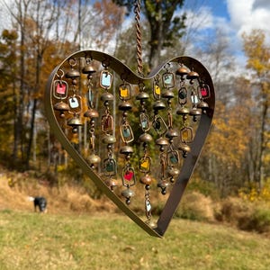 Handcrafted heart wind chime featuring colorful hanging dangles and decorative metal bells with a beautiful flamed finish. Metal wind chimes outdoor designed for garden decor, patio accents, porch decoration, balconies, fences, and backyard landscapes. Heart-shaped hanging garden ornament creates gentle, relaxing sounds while adding artistic charm to outdoor spaces. Perfect farmhouse decor, metal garden art, yard art, housewarming gift, romantic garden decor, and year-round outdoor decoration.