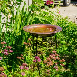 Hammered copper round birdbath with iridescent finish on curved metal stand.