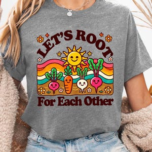 May include: Gray t-shirt with a graphic of a smiling sun and cartoon vegetables with the text "Let's Root For Each Other".