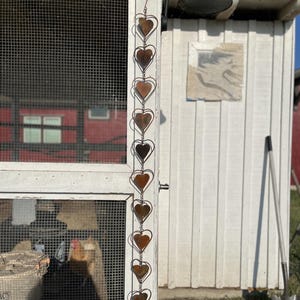 May include: A vertical hanging decoration featuring a series of ten interconnected metal hearts. Each heart is crafted from a thin wire outline surrounding a solid, weathered, copper-toned heart shape. The chain is suspended from a metal hook.