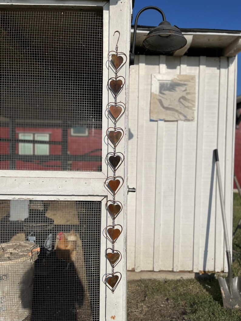 May include: A vertical hanging decoration featuring a series of ten interconnected metal hearts. Each heart is crafted from a thin wire outline surrounding a solid, weathered, copper-toned heart shape. The chain is suspended from a metal hook.