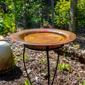 Hammered copper round birdbath with iridescent finish on curved metal stand.