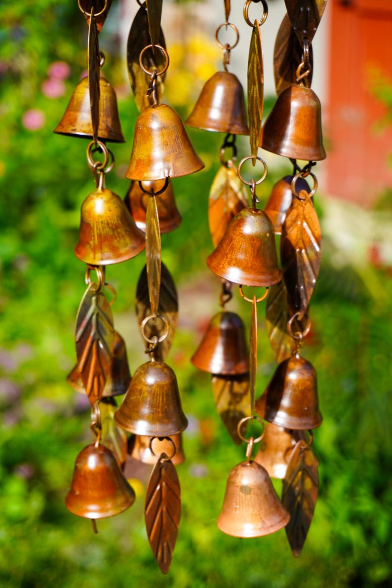 Puede incluir: Un carill&oacute;n de viento con m&uacute;ltiples campanas de metal de color cobre y colgantes en forma de hoja suspendidos de anillos circulares. Los componentes est&aacute;n dispuestos en hilos verticales, mostrando un acabado met&aacute;lico en tonos bronce y marr&oacute;n.