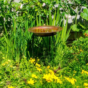Hammered copper round birdbath with iridescent finish on curved metal stand.