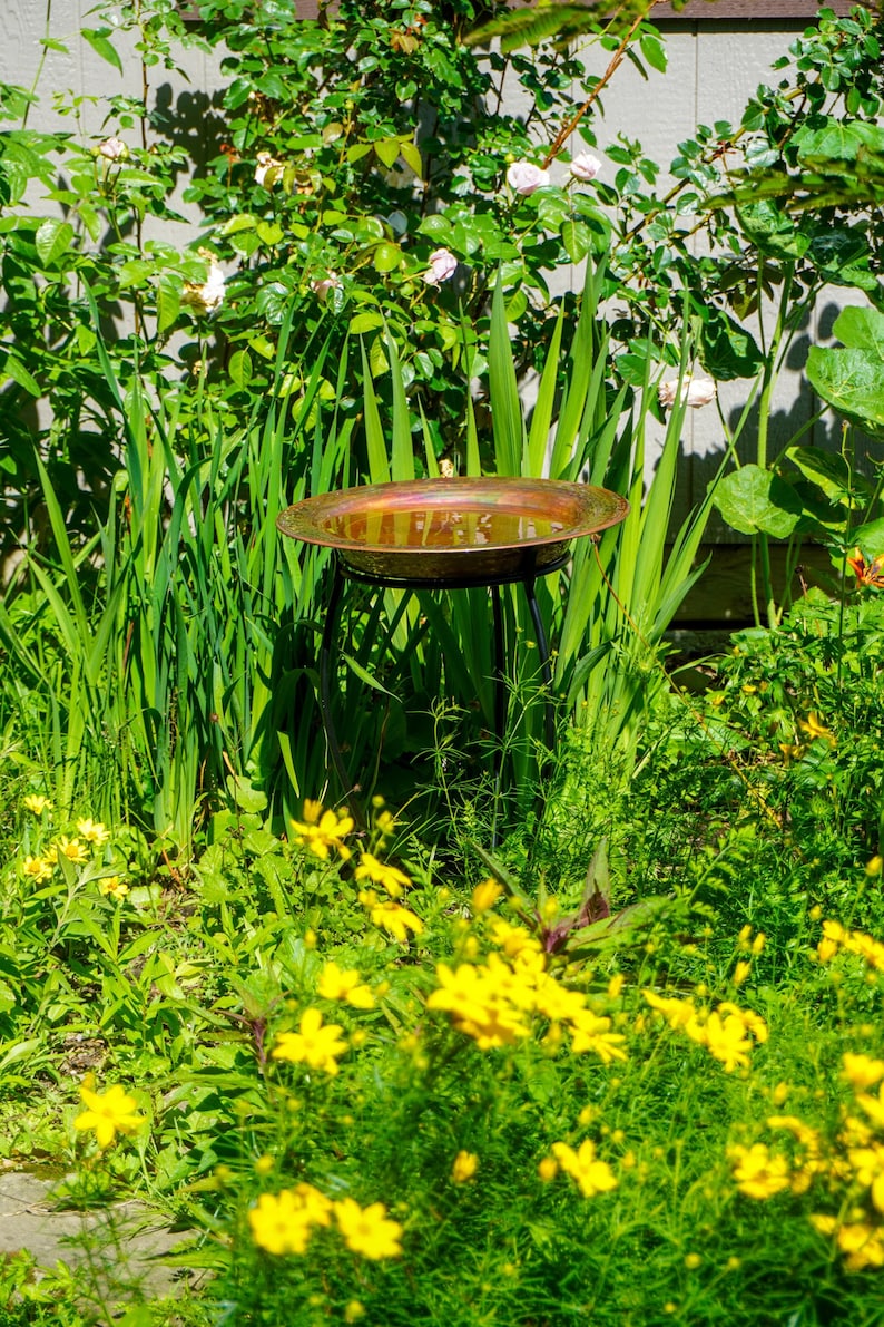 Hammered copper round birdbath with iridescent finish on curved metal stand.
