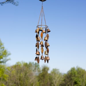 Single tiered metal wind chime with rustic copper finish featuring decorative hanging bells and leaf accents displayed in an outdoor garden setting. Handcrafted wind chimes outdoor for porch, patio, backyard, balcony, and garden decor. Metal wind chime adds soothing sounds and elegant movement to outdoor spaces. Rustic copper wind chime makes a beautiful gardener gift, gifts for mom, housewarming gift, outdoor garden decor, metal garden art, and yard decoration for every season.