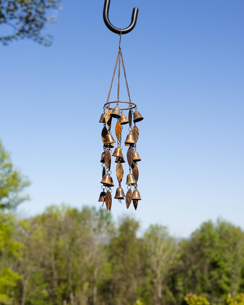 Single tiered metal wind chime with rustic copper finish featuring decorative hanging bells and leaf accents displayed in an outdoor garden setting. Handcrafted wind chimes outdoor for porch, patio, backyard, balcony, and garden decor. Metal wind chime adds soothing sounds and elegant movement to outdoor spaces. Rustic copper wind chime makes a beautiful gardener gift, gifts for mom, housewarming gift, outdoor garden decor, metal garden art, and yard decoration for every season.