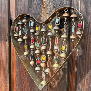 Handcrafted heart wind chime featuring colorful hanging dangles and decorative metal bells with a beautiful flamed finish. Metal wind chimes outdoor designed for garden decor, patio accents, porch decoration, balconies, fences, and backyard landscapes. Heart-shaped hanging garden ornament creates gentle, relaxing sounds while adding artistic charm to outdoor spaces. Perfect farmhouse decor, metal garden art, yard art, housewarming gift, romantic garden decor, and year-round outdoor decoration.