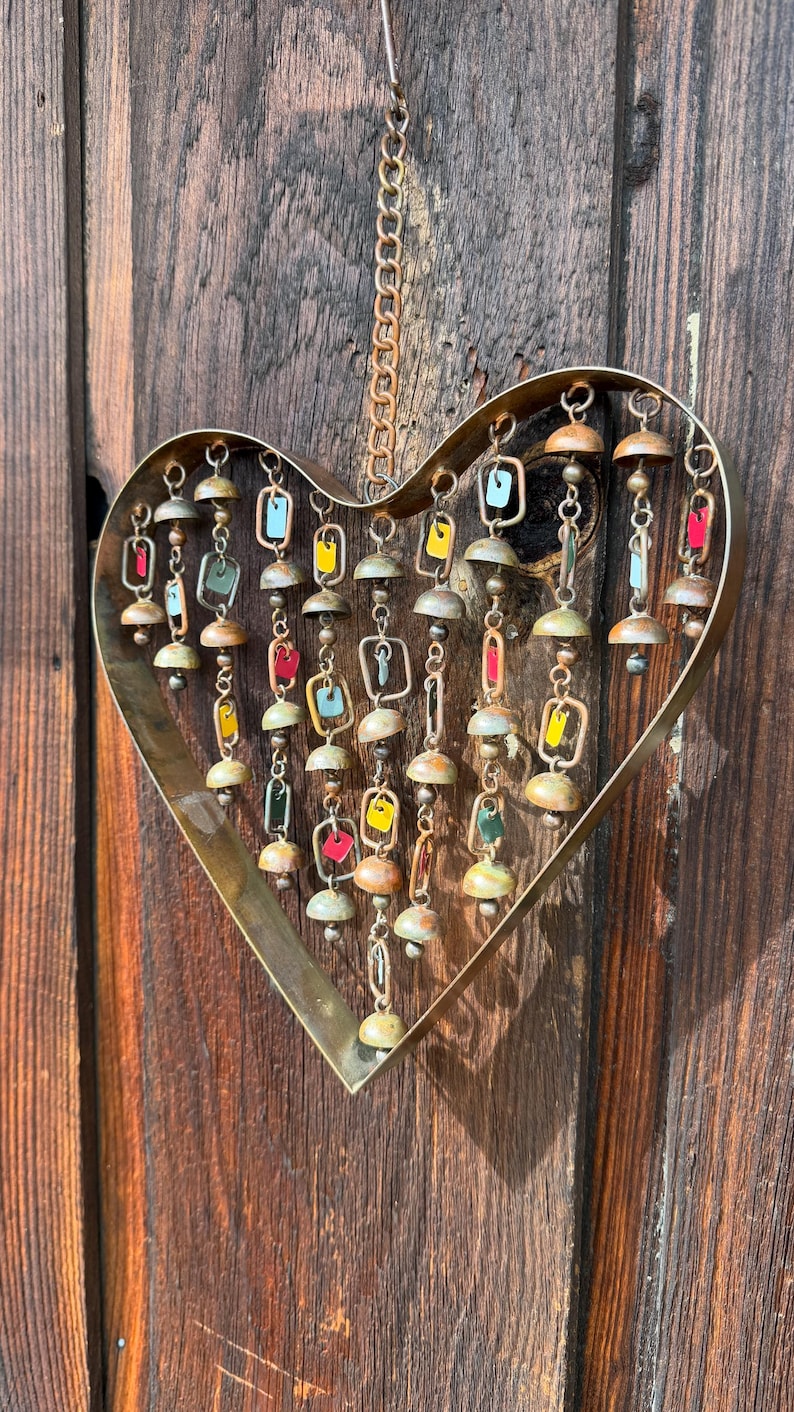 Handcrafted heart wind chime featuring colorful hanging dangles and decorative metal bells with a beautiful flamed finish. Metal wind chimes outdoor designed for garden decor, patio accents, porch decoration, balconies, fences, and backyard landscapes. Heart-shaped hanging garden ornament creates gentle, relaxing sounds while adding artistic charm to outdoor spaces. Perfect farmhouse decor, metal garden art, yard art, housewarming gift, romantic garden decor, and year-round outdoor decoration.