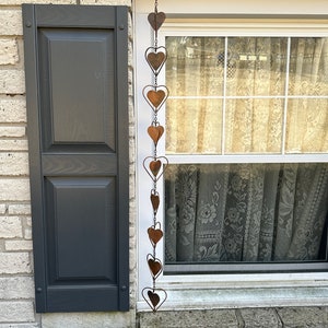 May include: A vertical hanging chain decoration composed of multiple interconnected copper-colored metal hearts. The hearts vary in size and are linked together by thin metal wire, creating a long, dangling ornament with a weathered, rustic finish.