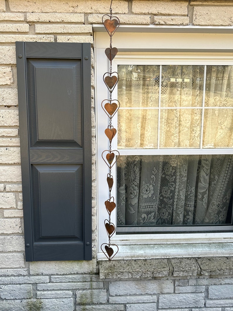 May include: A vertical hanging chain decoration composed of multiple interconnected copper-colored metal hearts. The hearts vary in size and are linked together by thin metal wire, creating a long, dangling ornament with a weathered, rustic finish.