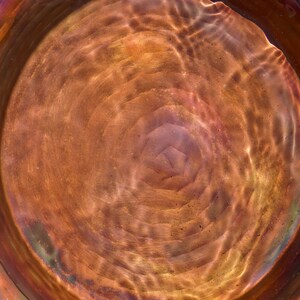 Hammered copper round birdbath with iridescent finish on curved metal stand.