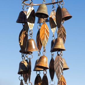 Single tiered metal wind chime with rustic copper finish featuring decorative hanging bells and leaf accents displayed in an outdoor garden setting. Handcrafted wind chimes outdoor for porch, patio, backyard, balcony, and garden decor. Metal wind chime adds soothing sounds and elegant movement to outdoor spaces. Rustic copper wind chime makes a beautiful gardener gift, gifts for mom, housewarming gift, outdoor garden decor, metal garden art, and yard decoration for every season.